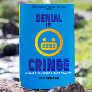 Denial is Cringe book in foreground. The book has blue background with large text Denial is Cringe Climate Pandemics Base Reality author name Jen deHaan. Book is being held in a nature environment.